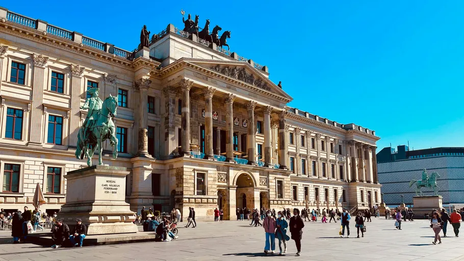 Historic building with equestrian statue, people walking.