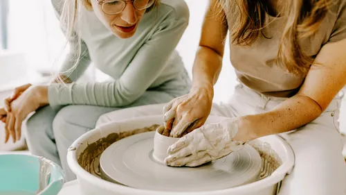 Two women crafting pottery on wheel indoors.