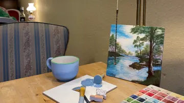 Painting supplies on table, landscape painting nearby.