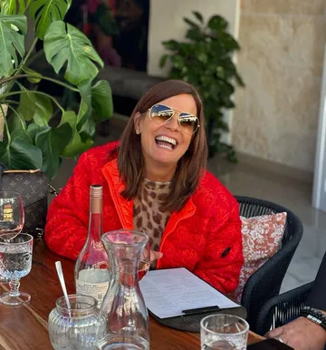 Smiling woman in sunglasses at outdoor table.