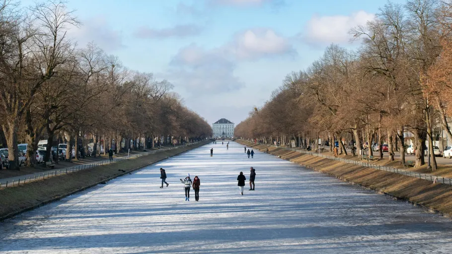 People walking on frozen canal, winter trees.
