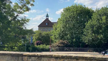 Altes Gebäude hinter Bäumen unter blauem Himmel.