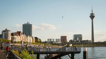Stadtansicht mit Turm und Uferpromenade.