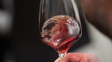 Person schwenkt Rotwein im Glas drinnen.