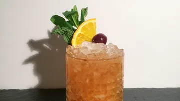 Cocktail mit Minze, Orange, Kirsche garniert.