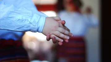 Verschränkte Kinderhände in traditioneller Kleidung.