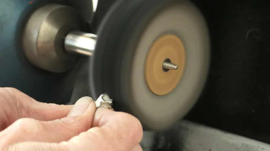 Hands polishing metal with a grinding wheel.