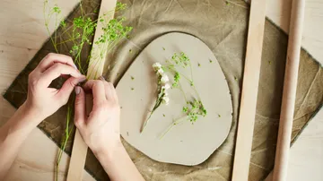 Hände basteln mit Pflanzen auf Tonscheibe.