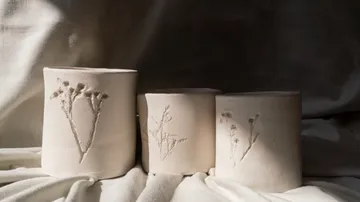 Drei Keramikvasen mit Blumendesigns, Stoff drapiert.
