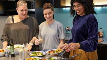 Drei Personen bereiten Essen in einer Küche vor.