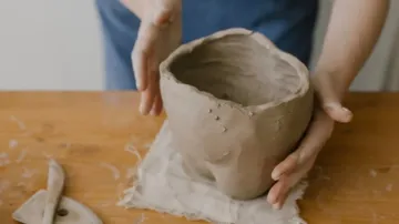 Hände formen Tontopf auf Holztisch.