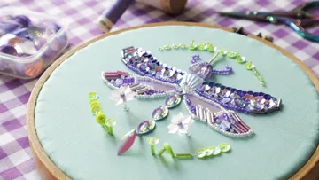 Beaded dragonfly embroidery on green fabric.