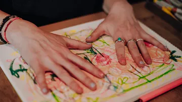 Hände erzeugen buntes Kunstwerk auf Papier.