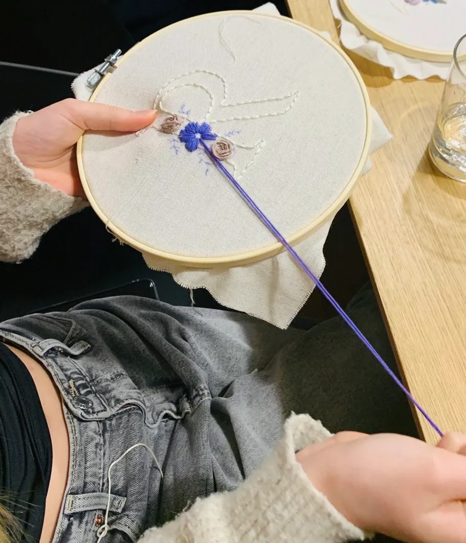 Hände halten Stickrahmen mit Blumendesign.