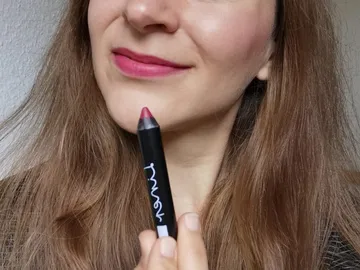 Woman holds lipstick in front of her face, smiles softly.