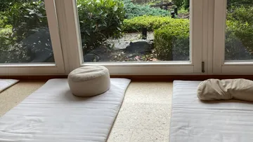 Meditationskissen auf Matten am Fenster.