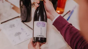 Person holding wine bottle with artwork label.