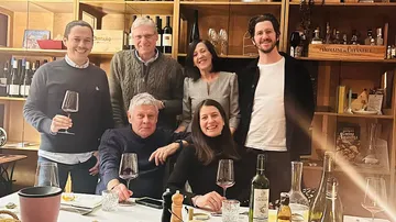 Six people smiling, holding wine glasses, in wine shop.