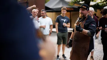 Mann in Schürze spricht draußen mit Gruppe.
