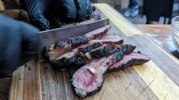 Person schneidet gegrilltes Steak auf Holzbrett.