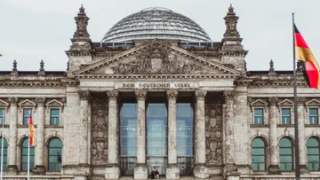 Reichstagsgebäude mit Fahnen, bewölkter Himmel.
