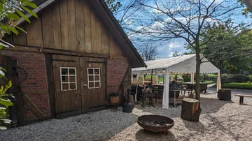 Rustic barn beside outdoor tent with trees nearby.