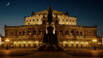 Beleuchtetes Opernhaus nachts mit Statue.