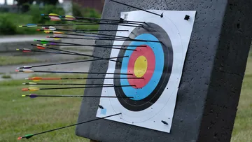 Pfeile treffen Bogenschießscheibe auf Rasenfeld.