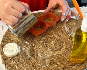 Hands pouring liquid into silicone molds on table.