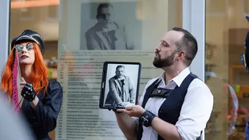 Person holds tablet with photo, another in costume.