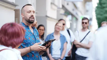 Mann spricht draußen zu Gruppe mit Tablet.