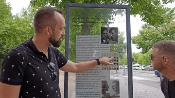Two men reading memorial information board outdoors.
