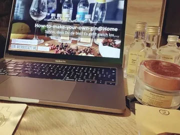 Laptop shows gin recipe surrounded by ingredients and bottles.
