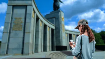 Frau nutzt Handy nahe großem Denkmal.