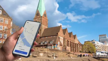 Hand hält Smartphone mit Karten-App, historische Gebäude dahinter.
