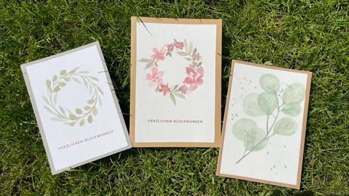 Three greeting cards on grass with floral designs.