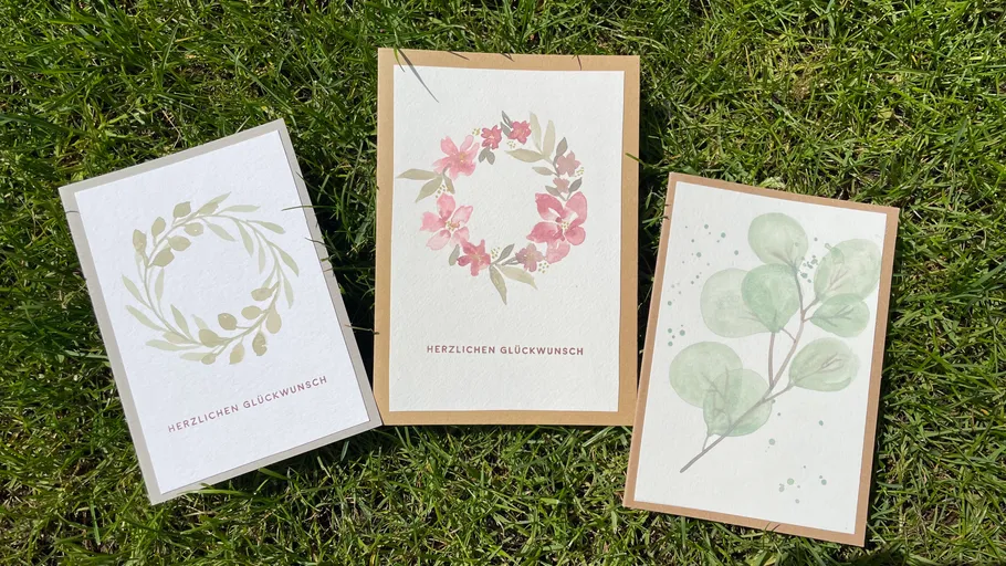 Drei Grußkarten auf Gras mit Blumendesigns.