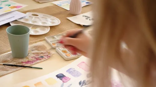Person painting at a table with supplies.