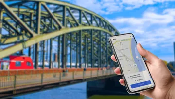 Hand hält Handy mit Karte, Brücke im Hintergrund.