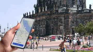 Hand hält Handy mit Karte vor Kathedrale.