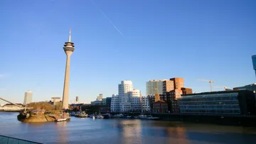 Rheinturm und moderne Gebäude am Fluss.