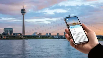 Hand holding phone, Düsseldorf tower background.
