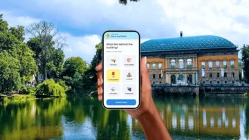 Hand holding phone with app, building in background.
