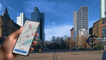 Hand hält Handy mit Karten-App, Stadtsilhouette.