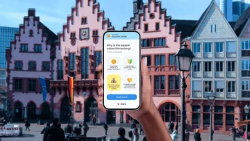 Hand hält Telefon auf historischem Stadtplatz.