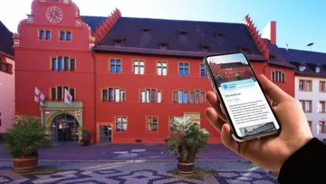 Person mit Smartphone vor rotem Gebäude.