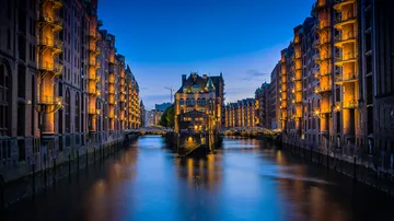Illuminated buildings reflecting on canal at dusk.