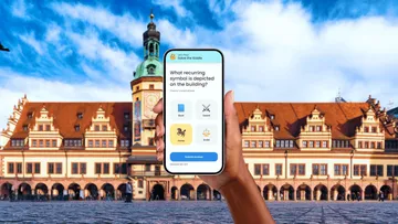Hand hält Telefon vor historischem Gebäude.