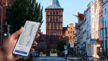 Hand hält Handy mit Karte, Stadtstraße im Hintergrund.