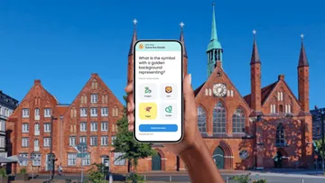 Hand hält Handy mit Quiz, historische Gebäude.